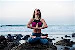 Young woman practicing lotus yoga pose on rocks at beach, Los Angeles, California, USA