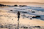 Silhouetted female runner running at sunset on beach, Los Angeles, California, USA