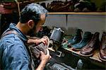 Male cobbler in traditional shoe workshop inspecting boot