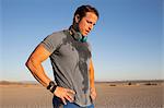 Man training, sweating with hand on hips on dry lake bed, El Mirage, California, USA