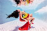 Woman underwater in swimming pool sitting on red plastic chair