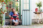 Sweden, Skane, Mossby, Daughter with father sitting on stone step and holding tablet pc