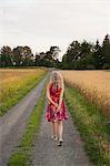 Sweden, Skane, Rear view of woman walking along dirt road in summer