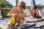 Sweden, Uppland, Runmaro, Barrskar, Boys (4-5, 6-7) repairing wooden deck in summer