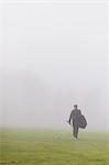 Sweden, Vastmanland, Teenage boy (14-15) walking in green field in fog