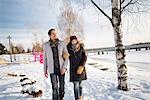 Sweden, Vasterbotten, Umea, Young couple walking in snow by river