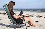 Sweden, Skane, Ahus, Teenage girl (16-17) using digital tablet on beach