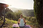 Italy, Tuscany, Dicomano, Woman in lotus position facing green hills