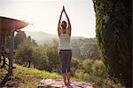 Italy, Tuscany, Dicomano, Woman practicing yoga against green hills