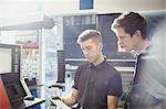 Workers reviewing paperwork at machinery control panel in steel factory