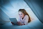 Smiling girl using digital tablet under sheet