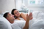 Smiling couple laying in bed using digital tablet