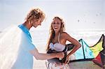 Man fastening kiteboarding safety harness on woman on sunny beach