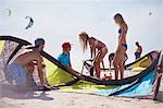 Friends preparing kiteboarding kite on sunny beach