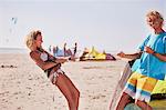 Playful couple preparing kiteboarding equipment on sunny beach