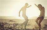 Playful couple dancing on sunny beach at sunset