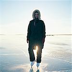 Sweden, Uppland, Varmdo, Bjorno, Mid adult woman in ice skates standing on frozen lake