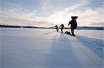 Sweden, Lappland, Jokkmokk, Three men cross-country skiing across frozen lake in winter