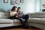 Sweden, Young couple sitting on sofa and looking at smart phone