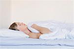 Finland, Helsinki, Portrait of young man sleeping in bed under white blanket