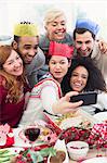 Friends in paper crowns taking selfie at Christmas dinner