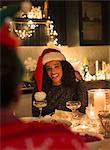 Smiling woman wearing Santa hat at candlelight Christmas dinner party