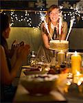 Enthusiastic woman serving cake with sparkler fireworks to clapping friends