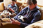 Boys using digital tablet and cell phone with puppies sleeping in laps