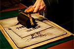 A sign maker rolling ink across the cut raised surface of linoleum preparing to print.