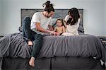 A young couple and their young son sitting together on their bed.