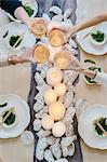 Overhead view of four people sharing a meal, plates of sushi and a table setting for a celebration meal.