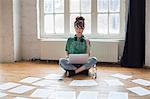 Young woman sitting on the floor in a rehearsal studio, using a laptop computer, looking at sheet music.