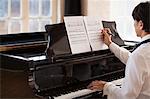 Young man sitting at a grand piano in a rehearsal studio, annotating sheet music.