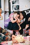 A family gathered to celebrate a one year old girl's birthday party. A cake with lots of candles.