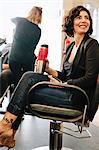 A woman client sitting in a hair salon chair, holding a mug of coffee.