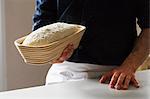 Close up of a baker holding a freshly baked loaf of white bread in a rattan proofing basket.