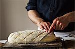 Close up of a baker slicing a freshly baked loaf of bread with a bread knife.