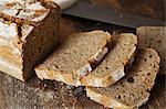 Close up of a loaf and slices of freshly baked bread on a wooden chopping board.