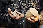 Close up of a man in a carpentry workshop, holding a wooden shape and wooden discs in his hands.