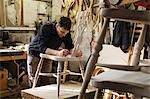 Man standing in a carpentry workshop, working on a wooden chair.