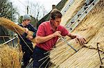 Two men thatching a roof, layering yelms of straw.