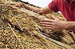 Close up of a man thatching a roof, layering the straw.