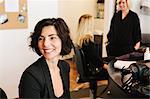 A client sitting at a hair salon, with two people in the background.