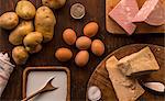 Overhead view of raw and prepared food, parmesan, milk, eggs and potatoes