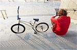 Rear view of man sitting on steps with BMX using smartphone