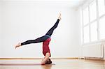 Woman in exercise studio legs apart doing headstand