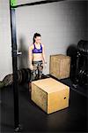 Young woman training, preparing to jump onto crate in gym