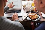 Over shoulder view of couple sitting at cafe table pointing at laptop