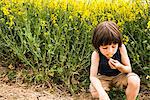 Boy crouching smelling yellow flower from field