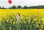 Portrait of boy standing in yellow flower field holding red balloon